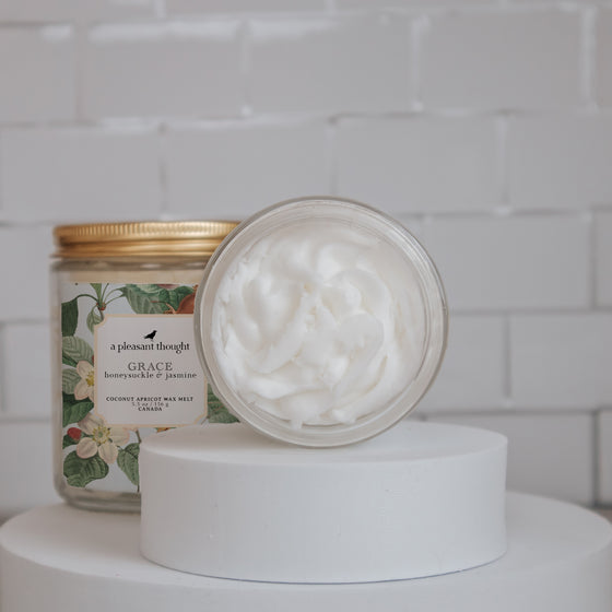 grace honeysuckle and jasmine Scoopable coconut apricot wax melt whipped into a clear glass jar with a gold lid and spoon open