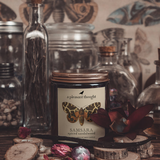 samsara spiced sandalwood coconut apricot wax candle in a classic, amber glass jar with a wooden wick and lid notes